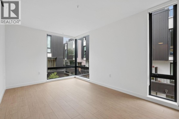 Empty room with light wood floors and large corner windows offering views of the exterior. - 221 2820 Nanaimo Street, Vancouver