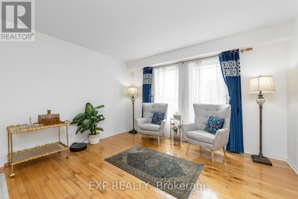 Living room with light gray armchairs, blue patterned curtains, hardwood floors, and a dark rug. - 221 Northwind Street, Ottawa