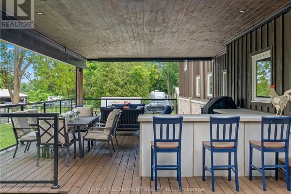 Covered deck with dining set, bar seating, grill, and glass railing - 2210 Highway 54 Haldimand