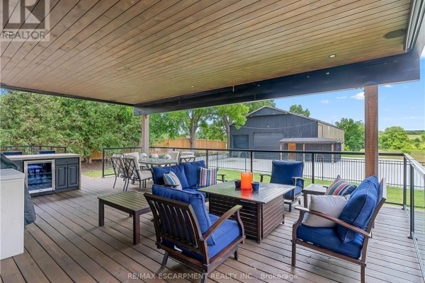 Covered deck patio with outdoor kitchen, seating, and dining area overlooking a barn - 2210 Highway 54 Haldimand