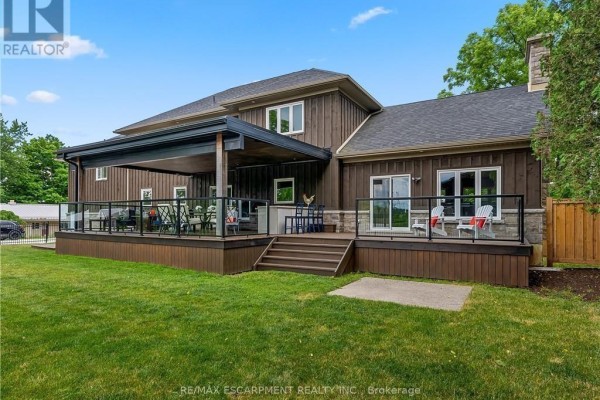Rear exterior view of the house showing a large wooden deck with glass railings and covered patio. - 2210 Highway 54, Haldimand