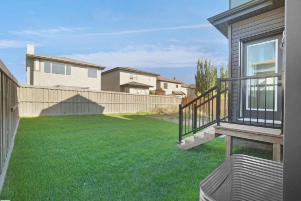 Backyard with a green lawn, wooden deck, metal railings, and a wooden fence. - 22108 94 Av Nw, Edmonton