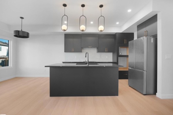 Open concept kitchen with a large dark island, stainless steel refrigerator, and pendant lighting. - 22108 94 Av Nw, Edmonton