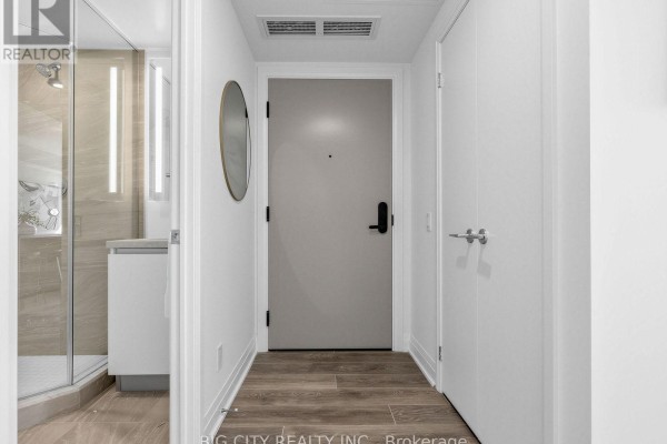 Apartment hallway with a gray door, round mirror, and open bathroom door on the left. - 2211 - 25 Frederick Todd Way, Toronto