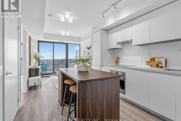Modern kitchen with white cabinets, island with seating, and view of the living room. - 2211 - 25 Frederick Todd Way, Toronto