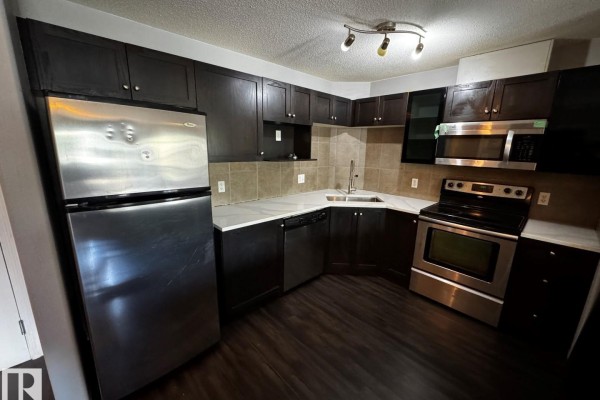Kitchen with dark cabinets, stainless steel appliances, beige tiled backsplash, and white quartz countertops. - #2211 9357 Simpson Dr Nw, Edmonton
