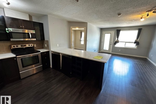 Open concept living and kitchen area with dark hardwood floors, grey walls, a white quartz island, and a balcony door. - #2211 9357 Simpson Dr Nw, Edmonton