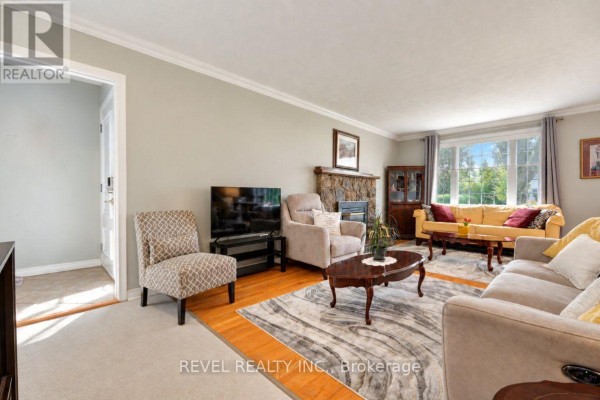 Living room with a stone fireplace, hardwood floors, large windows, and various seating arrangements. - 2213 Circle Place, Ottawa