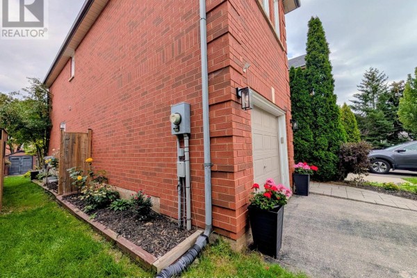 Side view of brick townhouse showing garage, electrical meter, and garden beds. - 2213 Ridge Landing, Oakville
