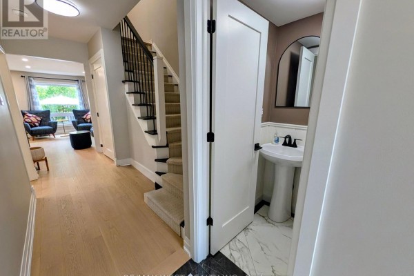 Hallway with light wood floors, carpeted stairs, and a doorway to a powder room. - 2213 Ridge Landing, Oakville