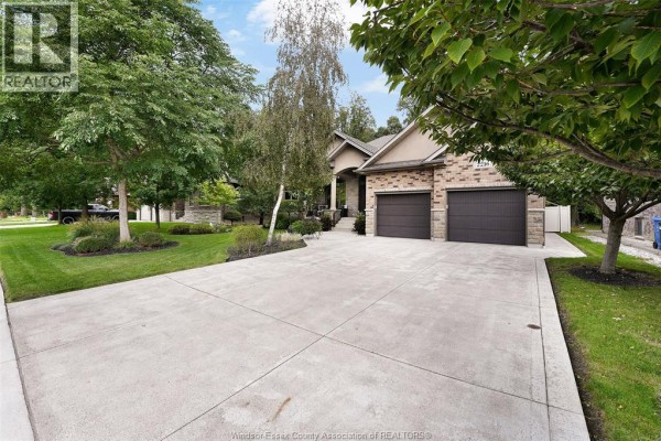 Concrete driveway leading to a brick house with two garage doors and mature trees. - 2216 Roxborough, Windsor