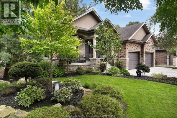 Landscaped front yard with lush green grass, shrubs, and a birdbath in front of house. - 2216 Roxborough, Windsor