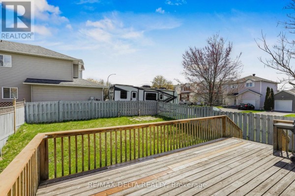 View from the deck of a backyard with grass, fence, and neighboring houses under a blue sky. - 2218 Cecile Crescent, Clarence Rockland
