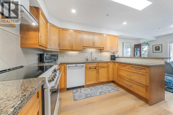 Kitchen with light wood cabinets, granite countertops, and stainless steel appliances. - 222, 6868 Sierra Morena Boulevard Sw, Calgary