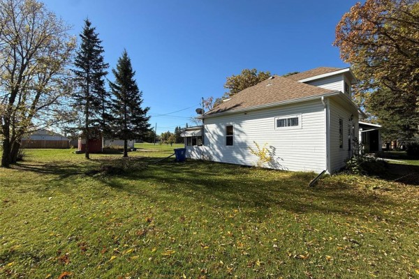 Side view of a white house with a brown roof, surrounded by green grass and mature trees. - 222 1st Avenue, Mccreary