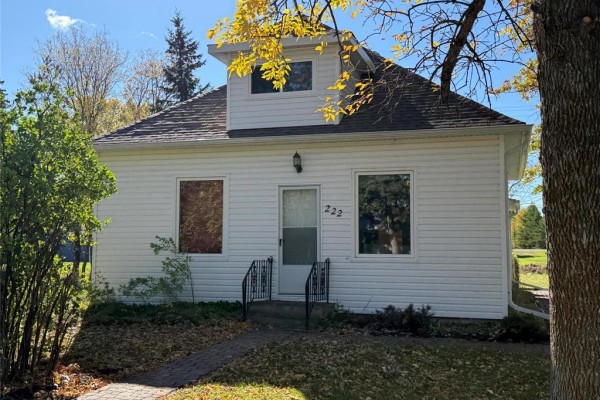 Front exterior of a white house with a peaked dormer window and a paved walkway to the door. - 222 1st Avenue, Mccreary