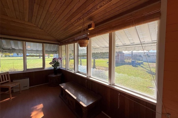 Sunroom with wood-paneled walls and ceiling, large windows, and a wooden chair and bench. - 222 1st Avenue, Mccreary