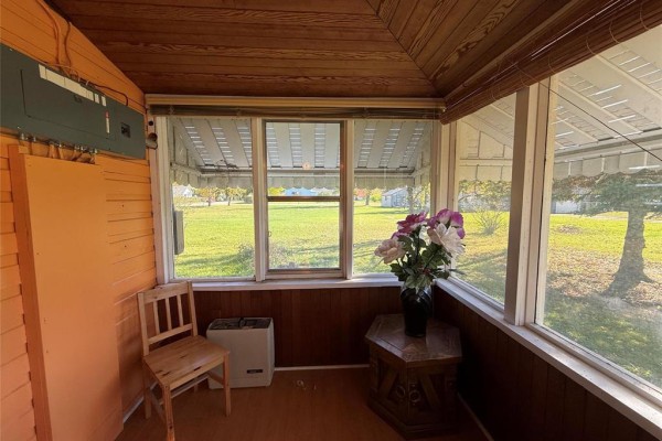 Sunroom interior with wood paneling, large windows offering views of the yard, and floral decorations. - 222 1st Avenue, Mccreary