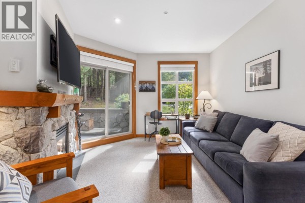 Living room with a large stone fireplace, a navy blue sofa, and a TV mounted above the fireplace. - 222 4660 Blackcomb Way, Whistler