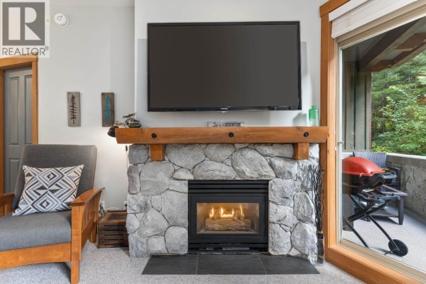 Living room with a navy blue sofa, stone fireplace, and a view of the dining area and kitchen. - 222 4660 Blackcomb Way, Whistler