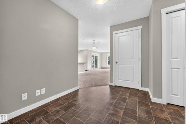 Apartment hallway entrance with dark tile flooring and light gray walls leading to living area. - #222 5810 Mullen Pl Nw, Edmonton