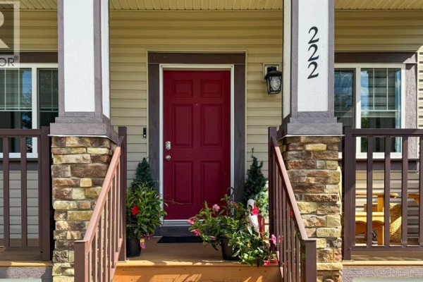 Entrance to the house with a red front door, decorative plants, and porch railings. - 222 Copperpond Boulevard Se, Calgary