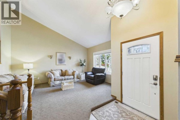 Living room with plush beige carpet, neutral walls, a white front door, and large window. - 222 Davison Drive, Red Deer