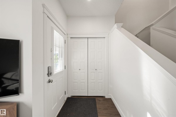 Interior entrance area with a white front door, double closet doors, and hardwood floors. - 222 Desrochers Bv Sw, Edmonton