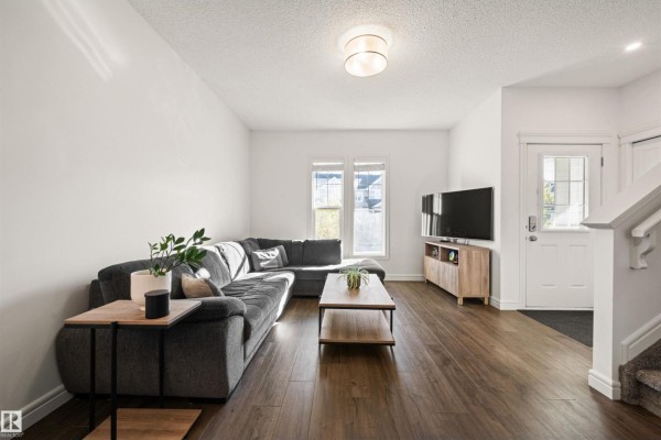 Living room with a grey sectional sofa, coffee table, entertainment unit, and a view of the front entrance. - 222 Desrochers Bv Sw, Edmonton