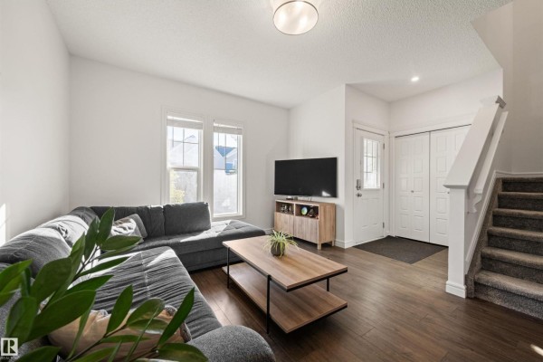 Living room with a large grey sectional, modern coffee table, and dark wood floors, open to the entrance. - 222 Desrochers Bv Sw, Edmonton
