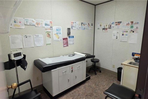 Second medical room with an exam table, sink, and patient educational materials. - 222 Fairview Drive Unit# 205, Brantford
