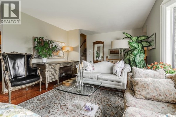Living room with a black armchair, ornate desk, sofa, and glass coffee table. - 222 Gathercole Crescent, Saskatoon