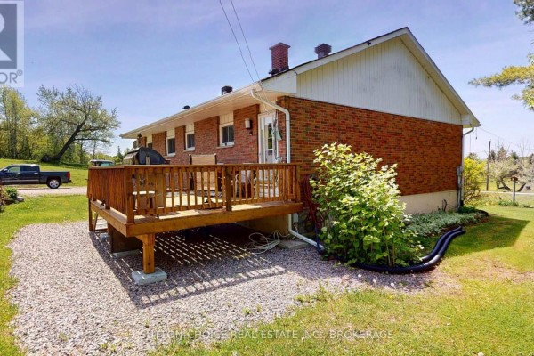 Rear view of the brick bungalow showing a wooden deck with seating and gravel landscaping. - 222 Yonge Street, Bonfield