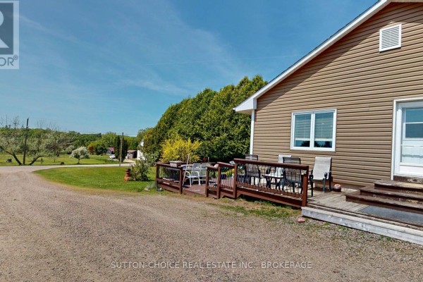 Deck with outdoor furniture attached to the side of the beige-sided house, overlooking a rural landscape. - 222 Yonge Street, Bonfield