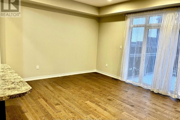 Empty living room with dark hardwood floors, beige walls, and a sliding glass door. - 2225 Tribalwood Street, London North
