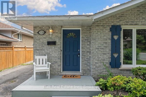 Close-up front door view of a bungalow with grey brick, blue door, and white chair. - 2226 Springwood Road, Peterborough