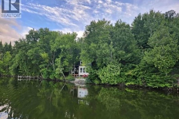 Aerial view of a white cottage nestled amongst dense green trees beside a calm body of water. - 223 Ch Beaulieu Road, Saint Francois De Madawaska