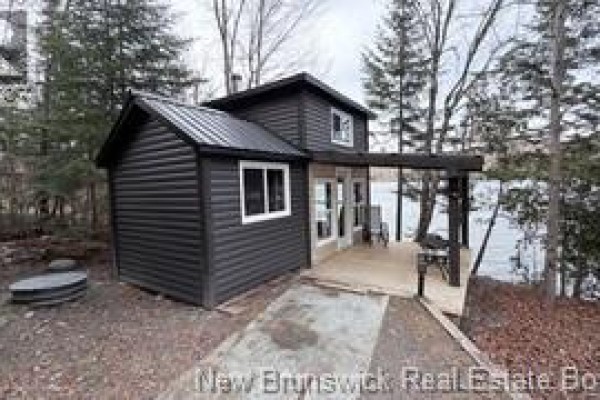 Exterior view of a small dark grey cottage with a metal roof and a covered wooden deck. - 223 Ch Beaulieu Road, Saint Francois De Madawaska