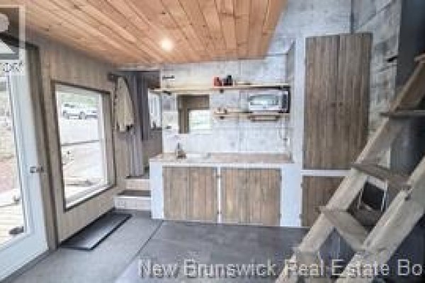 Interior view of a small kitchenette with concrete walls, wooden cabinets, and a ladder leading up. - 223 Ch Beaulieu Road, Saint Francois De Madawaska