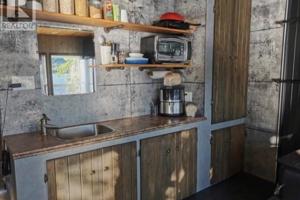 Close-up of a kitchenette with concrete walls, stainless steel sink, wooden cabinets, and shelves. - 223 Ch Beaulieu Road, Saint Francois De Madawaska