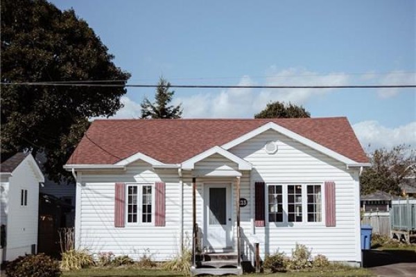 White vinyl siding and red roof of a bungalow on a sunny day. - 223 Dover Street, Campbellton