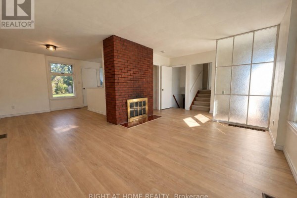 Spacious living room featuring a red brick fireplace, light wood flooring, and access to stairs. - 223 Ellendale Drive, Toronto