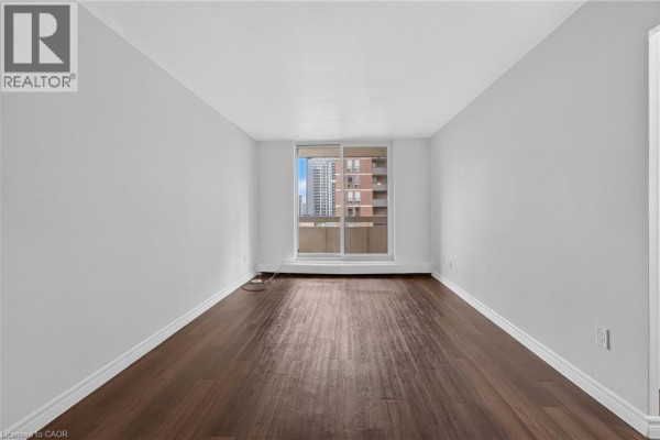 Empty room with dark wood floors and a large window with view of buildings. - 223 Jackson Street W Unit# 908, Hamilton