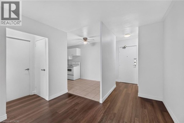 Hallway with dark wood floors leading to a kitchen with white appliances. - 223 Jackson Street W Unit# 908, Hamilton