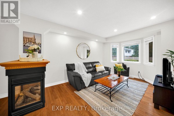 Living room with a black leather sofa, fireplace, coffee table, and wood floors. - 223 Monterey Drive, Ottawa