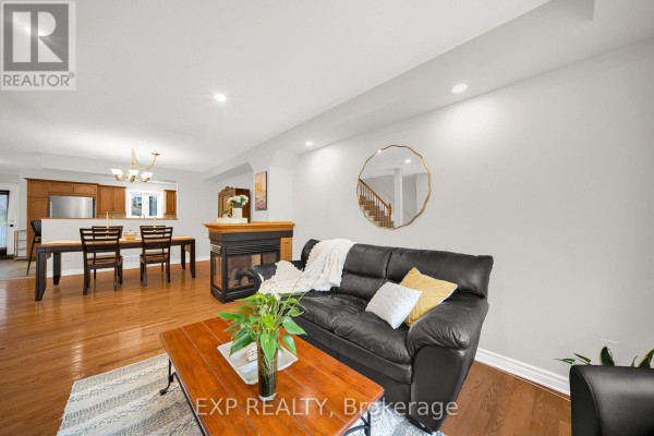 Living room with fireplace and view of dining area, kitchen, and staircase in background. - 223 Monterey Drive, Ottawa