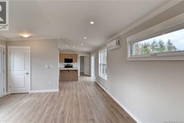 Interior view of an open-concept living and kitchen area with light wood laminate flooring and beige walls. - 223 Rue Bella Vista, Tracadie