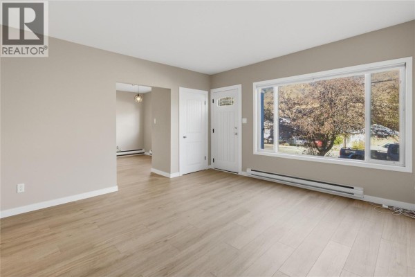 Living room with beige walls, light wood floors, and a large window overlooking trees. - 2231/2233 Valleyview Drive, Kamloops