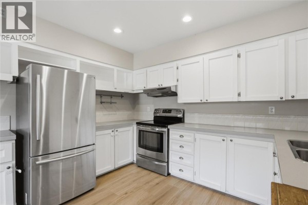 Close-up of a white kitchen with white cabinets, stainless steel appliances, and light wood floors. - 2231/2233 Valleyview Drive, Kamloops