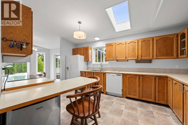 Kitchen with light wood cabinets, beige countertops, a kitchen island with stools, and a skylight. - 2233 6th St E, Courtenay